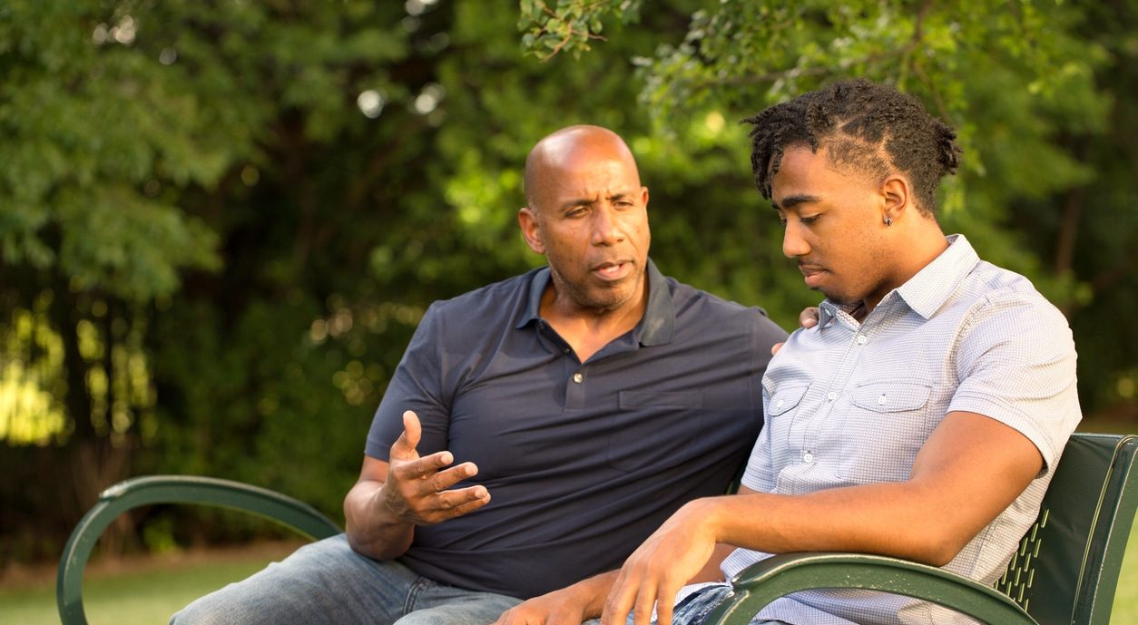Father navigating a critical conversation with son on a park bench.