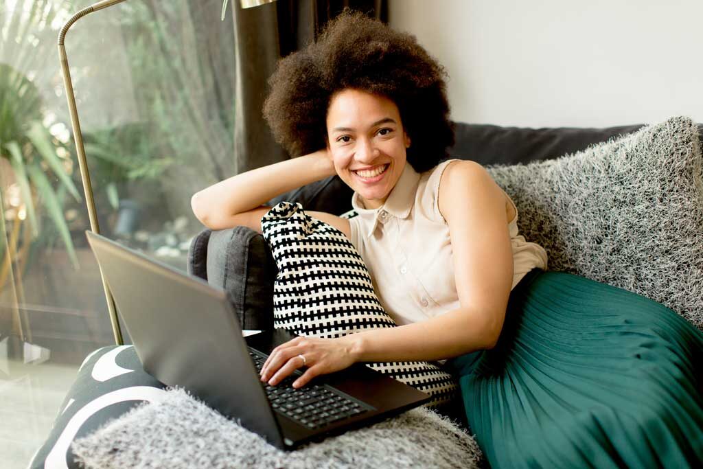 Young african american woman web-surfing internet and sitting on sofa