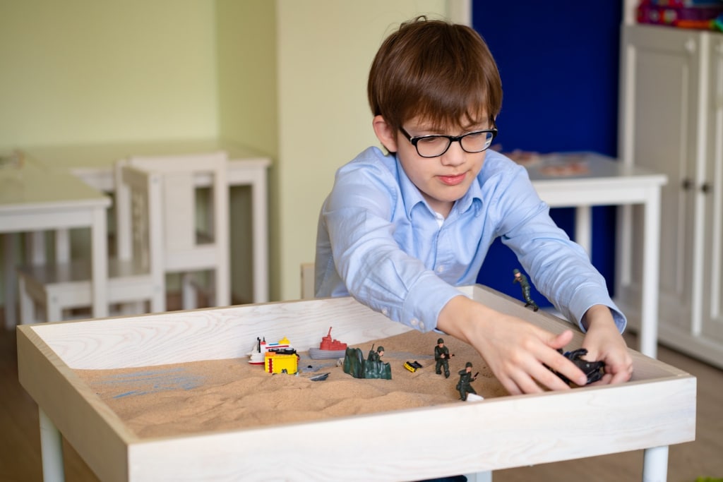 
		Child arranging miniature figures in a sand tray during a Jungian Sandplay activity		